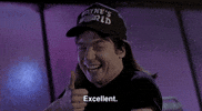 Movie gif. Mike Myers as Wayne in Wayne's World smiles as he looks at us and nods his head, giving a thumbs up. Text, "Excellent."