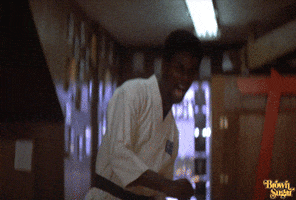 Video gif. A man in a martial arts uniform comes at us with a high kick and a fierce expression on his face. 