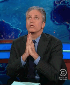 TV gif. Jon Stewart on The Daily Show looks up and kisses his hand, then raises it to the heavens while saying "Thank you," then uses his hand to draw a cross and a heart and then makes a groping gesture.