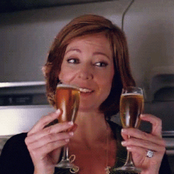 Movie gif As a flight passenger Allison Janney smiles while holding to full wine glasses and clinking them together