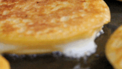 Video gif. Close-up of two golden tortillas crisping up on a griddle as white cheese oozes out of the sides.