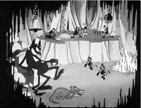 Disney gif. A vintage black and white cartoon of hell from Hell's Bells. The devil sits on a throne and taps his foot as little demons dance in front of him. A three headed dog sleeps at his feet and there’s a demon band playing several instruments while flames erupt in the corner. 