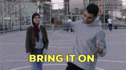 Video gif. On a basketball court, a man turns away from a woman, swinging his arm down as he smiles. Text, “Bring it on.”
