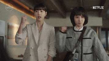 TV gif. Park Eun-bin as Young-woo and Ha Yoon-kyung as Su-yeon in Extraordinary Attorney Woo. Both of them are in the office reporting to a higher up and each of them pump a fist out in cheer and encouragement.