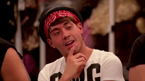 Reality TV gif. Phi Phi O'Hara in RuPaul's Drag Race is looking at something and thinking, tapping their finger on their lip.