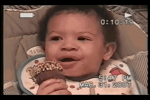 Video gif. In a home video dated March 31, 2007, a young baby grasps a Drumstick ice cream cone with a serious expression before bursting into laughter.