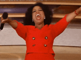Video gif. A less-than-a-second loop of Oprah Winfrey in a red jacket, holding her arms out and shouting excitedly. As there is little footage, she appears to be moving her head very fast.
