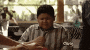 TV gif. Rico Rodriguez as Manny in Modern Family sits at a table during a family meal. Clearly distressed, he squeezes his eyes shut and performs the sign of the cross. 