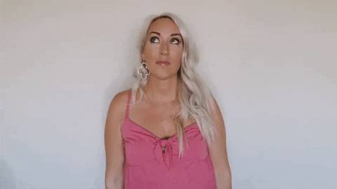 Video gif. Blond woman looks up and smiles, then points up with both of her hands.
