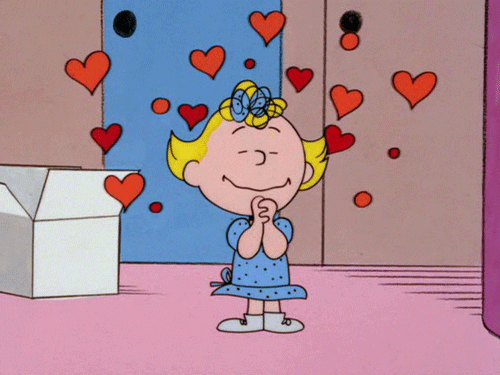 Cartoon gif. Sally from the Peanuts gang closes her eyes with her hands clasped together as she smiles and heart shapes dance around her head. 