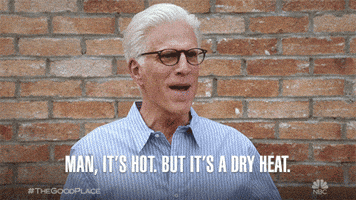 TV gif. Ted Danson as Michael in The Good Place optimistically says "Man, it's hot, but it's a dry heat."