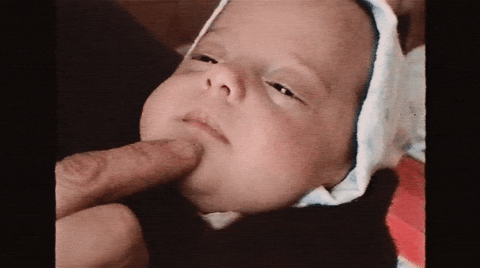 Video gif. Man pokes at a baby's cheeks and chin and the baby smiles slightly.