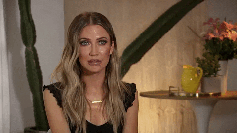 Reality TV gif. Bachelorette Kaitlyn Bristowe lowers her head, raises her shoulders, and grits her teeth in an awkwardly embarrassed smile. She then leans back and looks more at ease as she seemingly begins to explain herself.