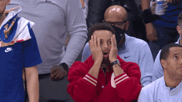 Sports gif. Steph Curry of the Golden State Warriors sits on the sidelines in street clothes, with his hands on his cheeks, looking up like he's looking at a scoreboard in utter disbelief.