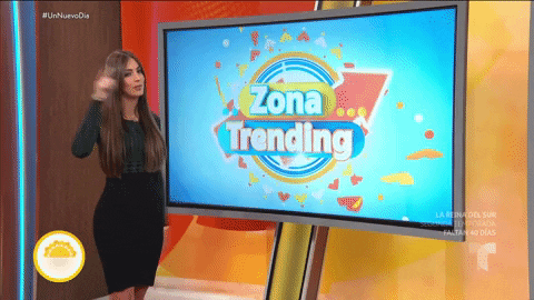 TV gif. Telemundo host Erika Csiszer thumps her chest and points toward us in front of a screen that reads, “Zona Trending.”