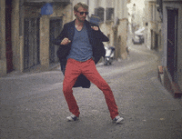 Video gif. Man dances in a brick-lined street waving his elbows and waggling his knees, the video distorted with an effect that make his body look noodlelike.