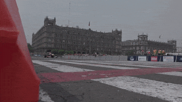 Sports gif. A formula 1 Red Bull car peels out and does donuts on the track. Then we see the same car speed past the finish line. 