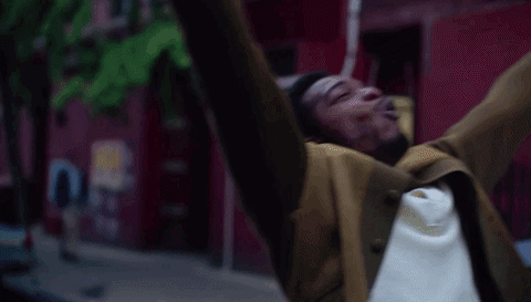 Movie gif. Stephan James as Alonzo Hunt in If Beale Street Could Talk stands in the middle of a city street at dusk, spreads out his arms, and screams "woo!" to the sky, as if a heavy burden has been lifted off his shoulders.