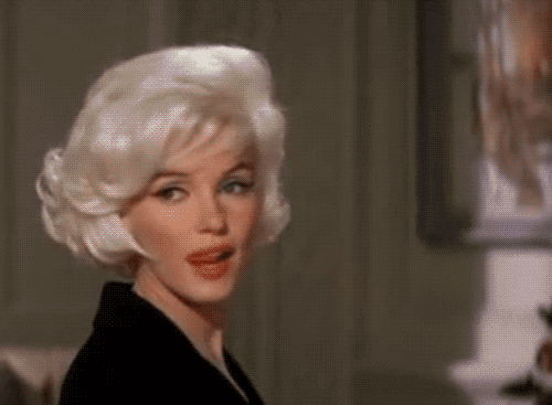 Movie gif. In slow-motion, Marilyn Monroe licks her lips as she turns toward us.