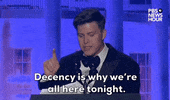 Video gif. Saturday Night Live's Colin Jost stands at a podium at the 2024 White House Correspondents' Dinner and delivers a sincere, serious statement. He says "Decency is why we're all here tonight," as he looks around the room with a serious expression.