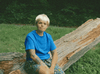 Meme gif. A person in a blonde wig and blue T-shirt sitting on a log, mimicking the Kazoo Kid meme, smiles and says, "I just wanted to say thanks, partner."