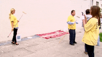 Reality TV gif. Paris Hilton on The World According To Paris. She's about to help paint a wall but poses for a picture with the brush first, popping a leg up and showing off her heels.