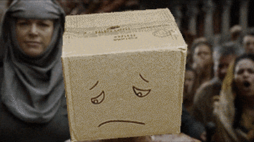 Meme gif. Medieval-looking crowd of people shouting shame behind a beaten-up man, whose head is superimposed with a cardboard box with a sad face drawn on it.