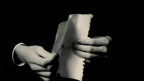 Video gif. Black and white shot of two hands spreading open a crinkled sheet of paper that reads, "I love you."