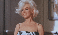 Celebrity gif. Marilyn Monroe gracefully flips her head of luscious blonde hair back while wearing a floral black and white, spaghetti strap dress.