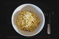 Video gif. Bowl of ramen noodles begins to fill up with soup, veggies, meat, and condiments.