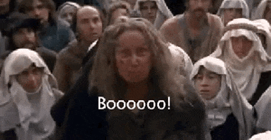 Movie gif. Margery Mason as the Ancient Booer in The Princess Bride stands up in front of a crowd of peasant people and looks up angrily at someone as she yells, “Boooooooo!”