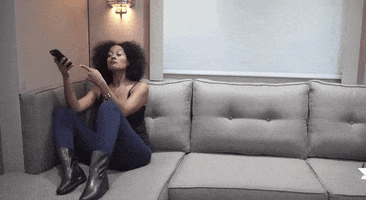 Celebrity gif. Tracee Ellis Ross sits on a couch while looking at her phone. She points her phone and then looks at us with wide eyes.