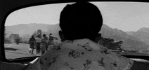 Movie gif. Black-and-white scene of a small child, Masahiko Shimazu as Shinichi in "High and Low," peering out the back window of a car as it drives away.