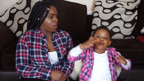 Video gif. Young girl in pink and purple flannel blows us a kiss while her mother, who is also wearing flannel, looks at her judgmentally.