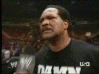 Sports gif. Wearing a black shirt that says “Damn,” WWE star Ron Simmons says into a microphone to a stadium full of people, “Damn!”