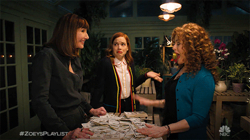 TV gif. Mary Steenburgen as Maggie, Bernadette Peters as Deb, and Jane Levy as Zoey on Zoey's Extraordinary Playlist are all gathered around a table of cash and Maggie and Deb high five one another excitedly.