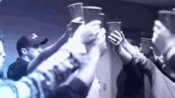 Video gif. Group of people have cups in the air and they toast one another before a Luke Bryan concert.