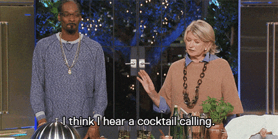 Reality TV gif. Snoop Dogg and Martha Stewart stand behind a countertop in "Martha and Snoop's Dinner Party"; Snoop bites his lip while Martha turns toward him slightly and says, "I think I hear a cocktail calling," which appears as text.
