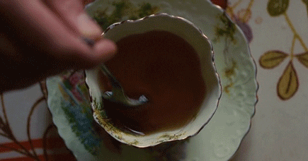 Video gif. Overhead shot of a person stirring tea in a fancy teacup.