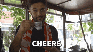Sports gif. Eli Mengem raises a teacup and smiles. Text, "cheers."
