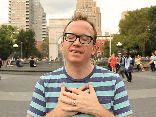 Celebrity gif. Chris Gethard standing in a city park with both hands over his chest, offering a heartfelt "thank you."
