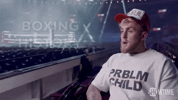 Sports gif. Jake Paul sits in an arena and mouths the words "boxing history". He's wearing a white shirt that reads "problem child". Text, "Boxing history".