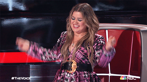 Reality TV gif. Kelly Clarkson on The Voice dances joyfully, smiling.