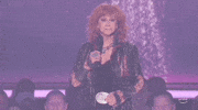 TV gif. Reba McEntire on stage at an awards show. She is wearing a black outfit with a silver belt buckle and a black jacket. The caption at the bottom of the gif first reads, “Okay?” Then, “Okay.” as she playfully seeks the audience’s approval.