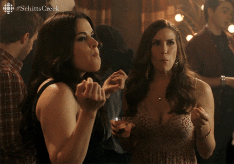 Schitt’s Creek gif. Sarah Levy as Twyla and Emily Hampshire as Stevie smile as Stevie raises her arms and shakes her head questioning. Text, "Where were you?"