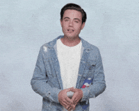 Celebrity gif. Wearing a denim jacket and a white shirt, Luke Cosgrove gives us an grimacing apology with hands clenched together. He turns up his hands and text appears, "Sorry."