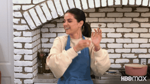 Reality TV gif. Selena Gomez on Selena and Chef waves her arms in the air in celebration.  