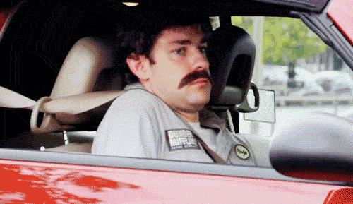 The Office Gif. John Krasinski as Jim Halpert sits in the passenger seat of a car. He wears a fake mustache and a Dunder Mifflin Warehouse uniform as if he’s in disguise. He looks out the window with a look of shame and slides the back of his seat down so he slowly disappears from view. 
