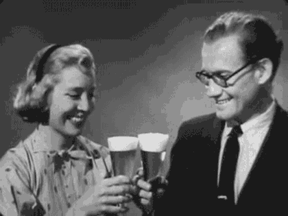 Video gif. Old black and white footage of a man and a woman smiling and clinking their glasses of beer, then raising the glasses to us.