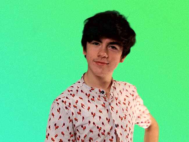 Celebrity gif. Declan McKenna smiles, a hand on his hip, and waves to us. 